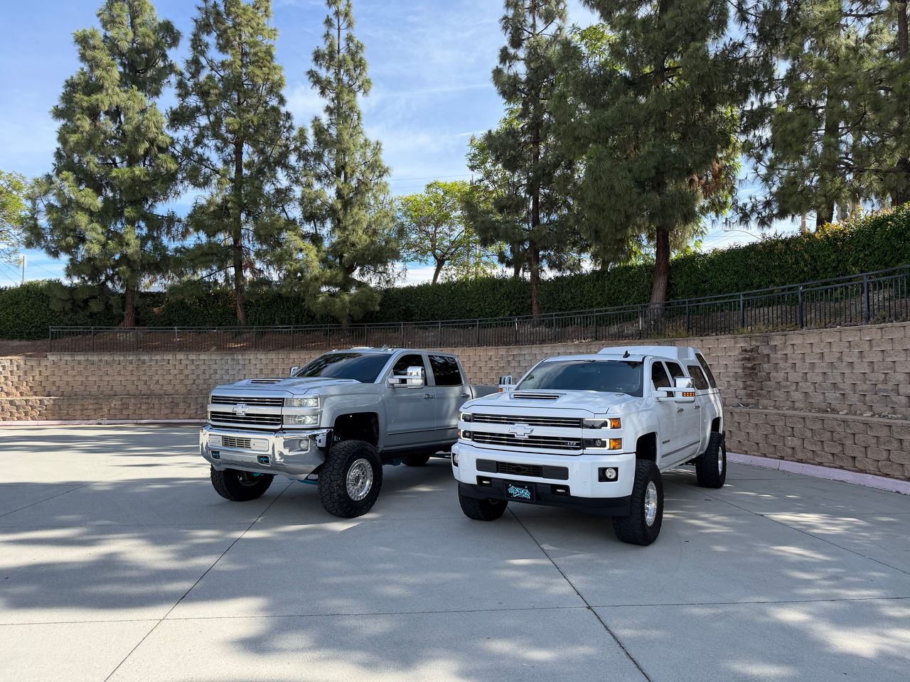 A lifted silver and a lifted white Chevrolet Silverado parked side by side.